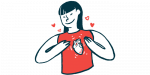 A woman smiles while gesturing to an heart pictured on her shirt.