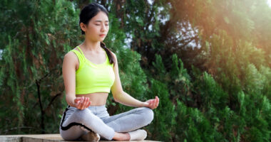 a woman in sportswear practicing meditation while sitting in the lotus position on a wall